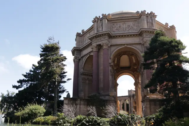 The ornate rotunda of the Palace of Fine Arts framed by cypress trees.