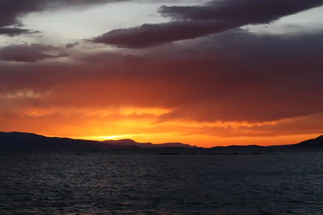 An orange sunset glowing under dark clouds above a mountain ridge and a dark sea.