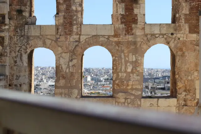 Three arched windows in the brick and stone wall of the Odeon of Herodes Atticus, the city spread out beyond them.