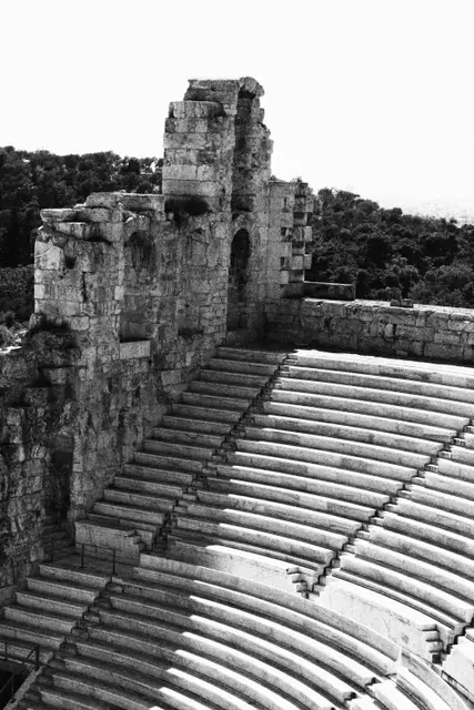 Black and white: the steep marble tiers of the ancient theater below a ruined stone wall.