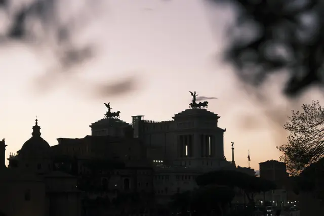 The Vittoriano and church domes in silhouette against a pink sky, framed by out-of-focus leaves.