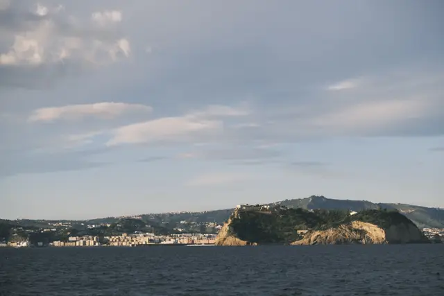 A tuff headland with houses on top, seen across dark water from the hydrofoil.