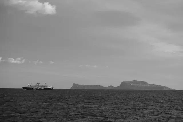 A car ferry crossing in front of the long silhouette of Capri.