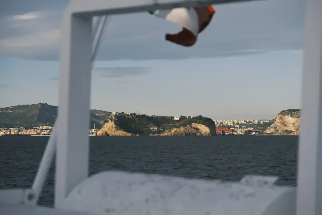 An Italian flag over the hydrofoil's white rail, a pale headland beyond.