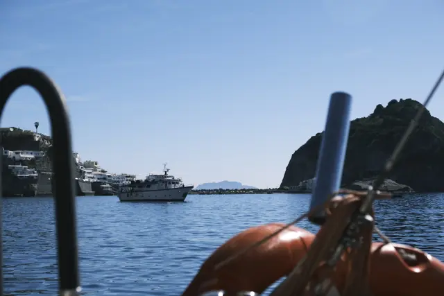 The bow of a small boat with an orange life ring, heading for Sant'Angelo's white houses and rock.