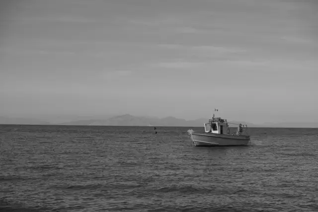 A small fishing boat at anchor, mountains faint on the horizon.