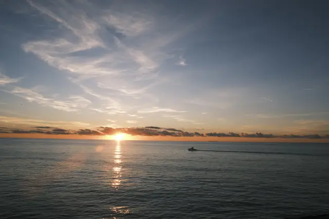The sun setting into the sea, a boat crossing its reflection.