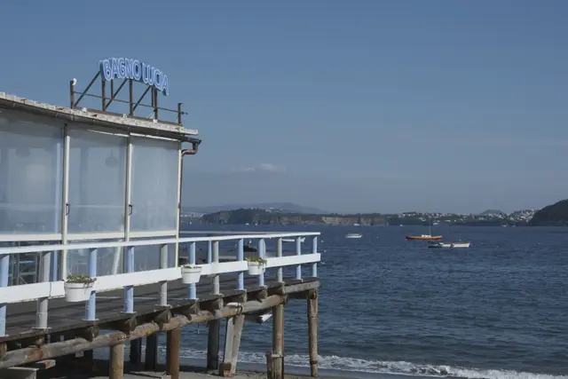 A beach club with a neon Bagno Lucia sign on a pier over the water.
