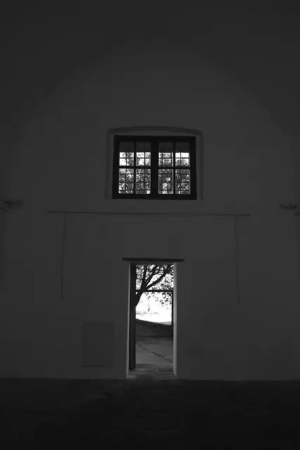A dark whitewashed wall, a window above a doorway onto a sunny courtyard.