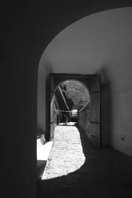 A shadowed arched tunnel leading to a sunlit gate.