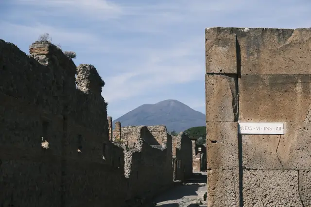 A street of ruined walls with Vesuvius at the end and a sign reading REG VI INS XII.