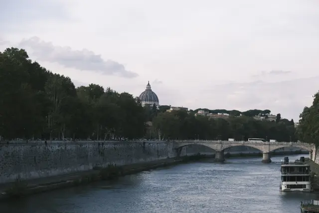 The Tiber in evening light, St Peter's dome above the trees, a bridge downstream.