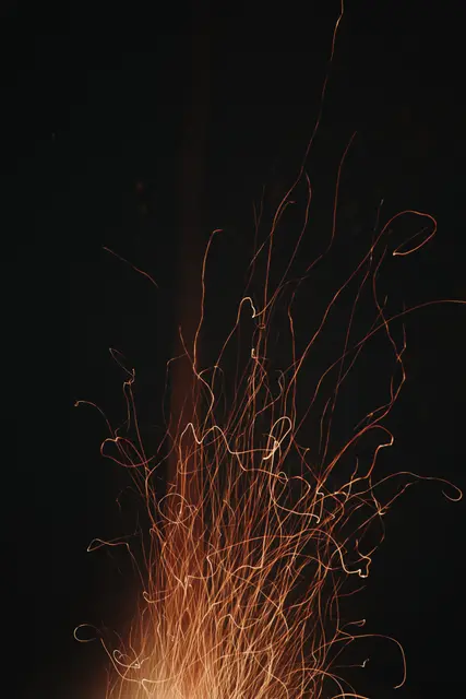 Sparks from a fire curling upward in fine orange threads against black.