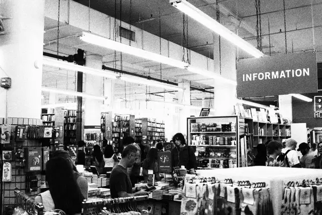 Black and white: shoppers browsing tables in a big bookstore under an Information sign.