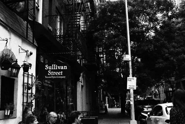 Black and white: a shop sign reading Sullivan Street Tea and Spice Company under fire escapes, people sitting out front.