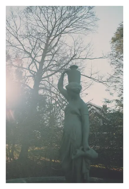 A stone statue of a woman beside bare trees, soft winter light behind it.