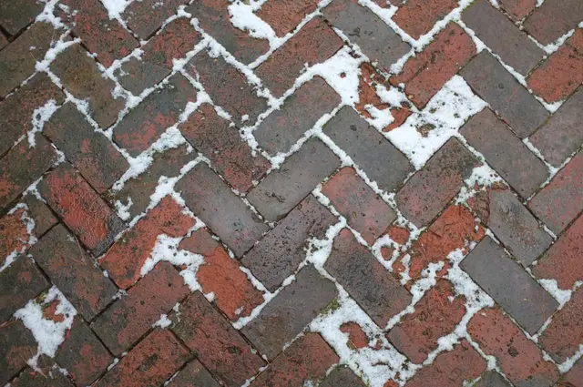 Red herringbone brick paving with snow caught in the joints.