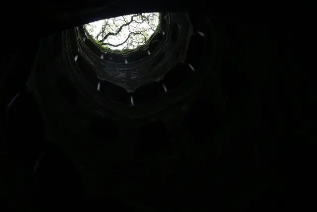Looking straight up the dark spiral of the Initiation Well to a circle of trees and daylight.