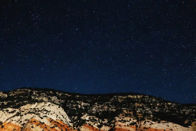 A night sky full of stars above pale and red cliffs.