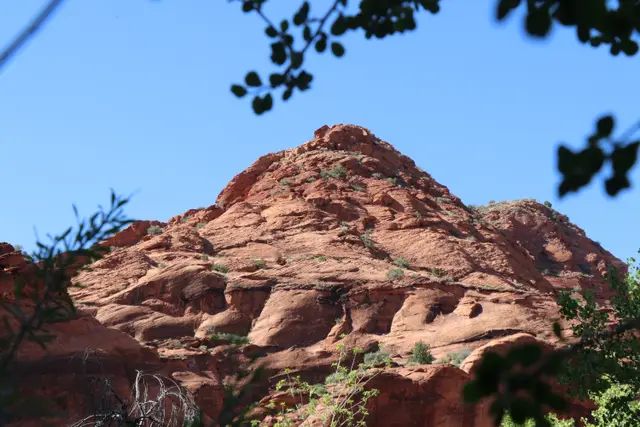 A red sandstone peak against blue sky, dark leaves framing the top.